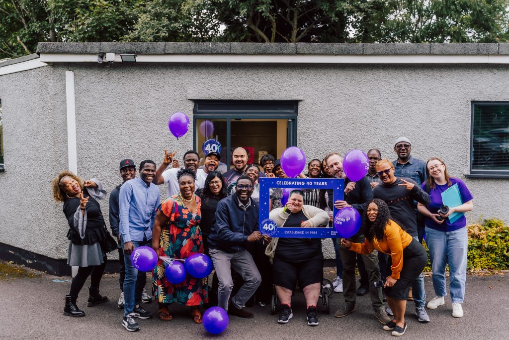 Large group of people pose in front of Birmingham office, smiling, with purple balloons