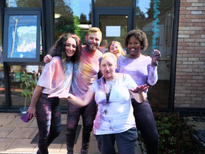 Group of people smiling in white t-shirts covered in colourful powder after a colour fight